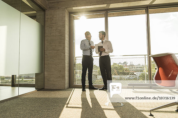 Two young businessmen talking at the window in office