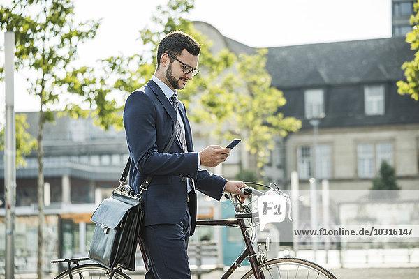 Junger Geschäftsmann schiebt Fahrrad  hält Smartphone