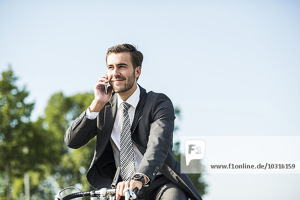 Ein junger Geschäftsmann  der Fahrrad fährt und telefoniert.