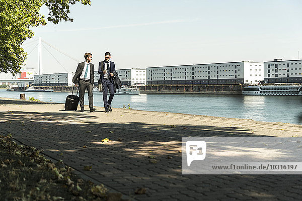 Two young businessmen on a business trip  walking by river