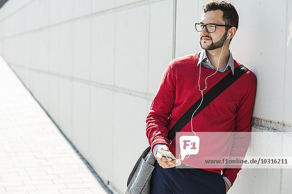 Young businessman using smart phone  wearing ear phones