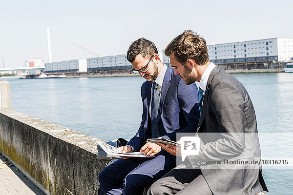 Zwei junge Geschäftsleute  die an der Wand am Fluss sitzen und arbeiten.