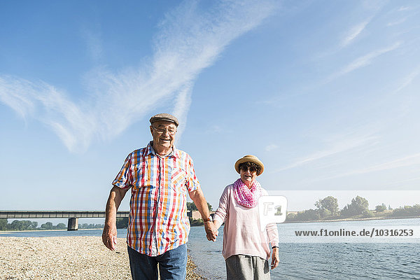 Deutschland  Ludwigshafen  glückliches Seniorenpaar  das Hand in Hand am Flussufer spazieren geht.