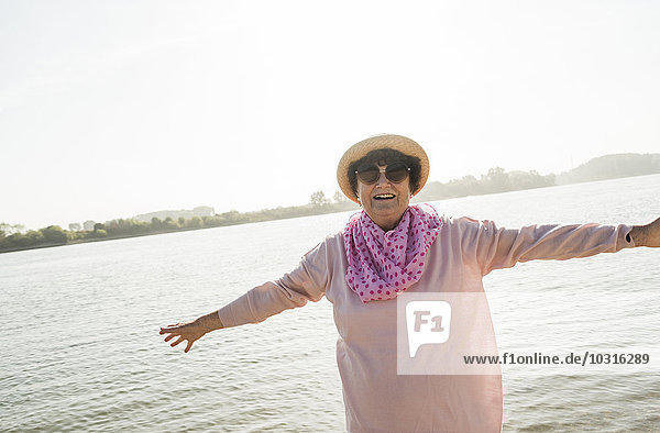 Porträt einer lächelnden Seniorin mit ausgestreckten Armen vor einem Fluss