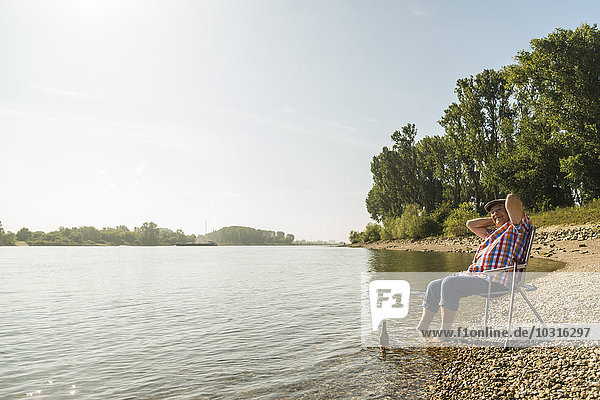 Deutschland  Ludwigshafen  fröhlicher Senior entspannt auf Klappstuhl am Flussufer