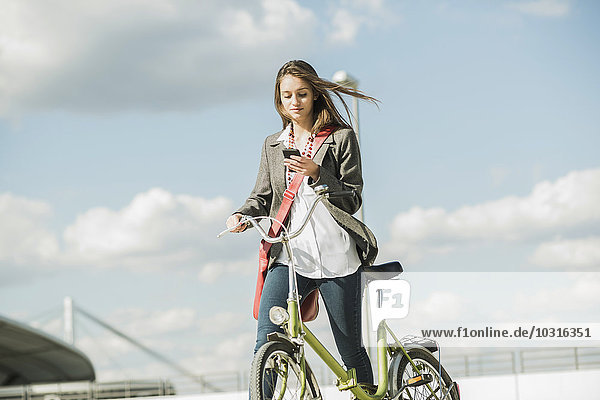 Junge Frau mit Fahrrad beim Blick aufs Handy
