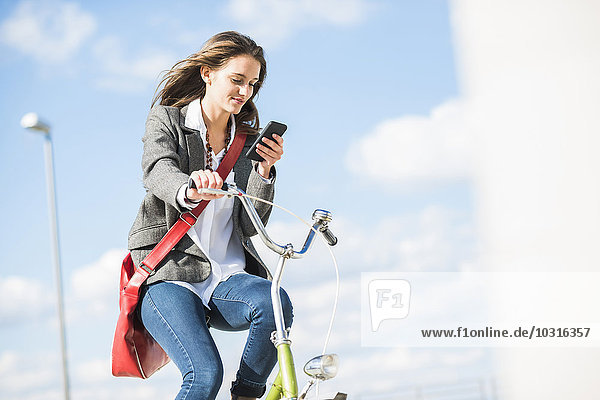 Young woman on bicycle looking at cell phone