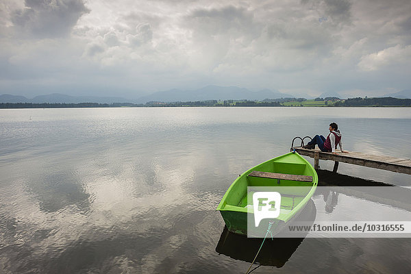 Woman sitting on pier  Hopfensee lake  green rowing boat