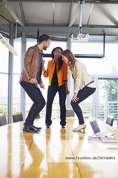 Three happy creative people dancing on a conference table