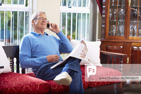 Senior man on the phone reading newspaper at home