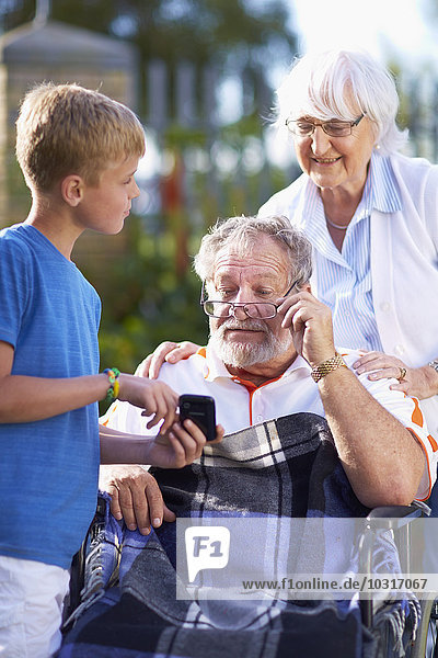 Grandmother and grandson explaining cell phone to grandfather in wheelchair