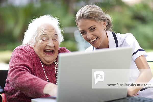 Glückliche Krankenschwester und Seniorin mit Laptop zusammen