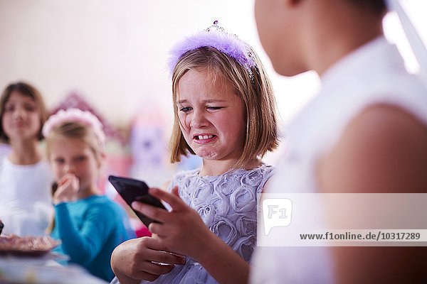 Girl with cell phone on a birthday party pulling a face