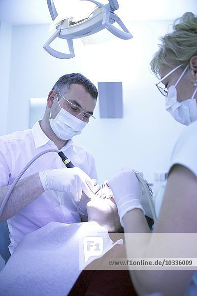 Zahnbearbeitung eines Patienten durch Zahnarzt und Assistentin