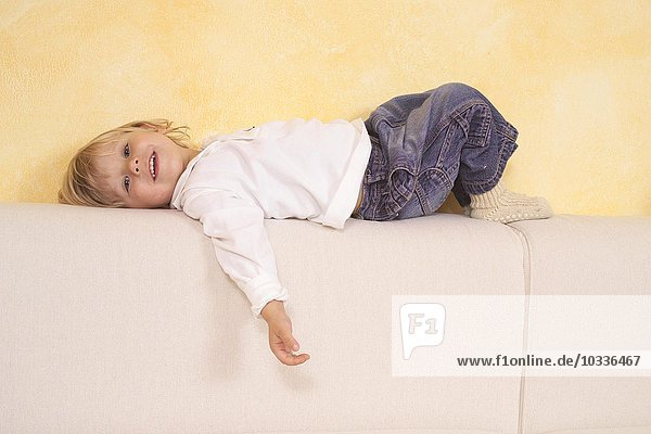 Kind liegt auf einem Sofa und lacht
