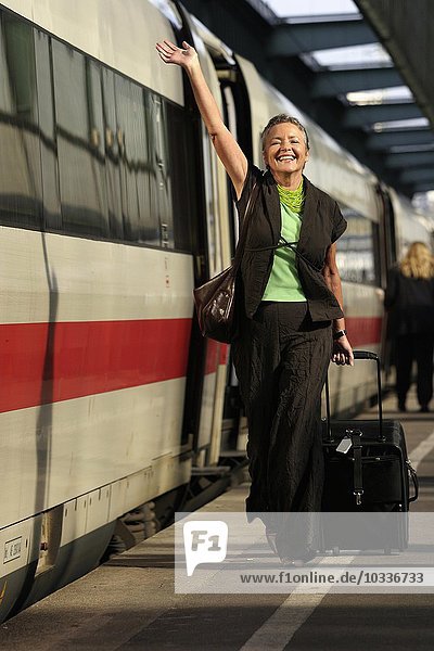 Ältere Frau mit Trolley winkt auf dem Bahnsteig