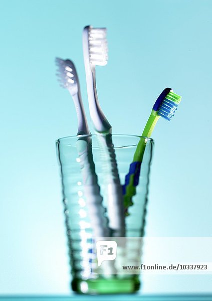 Glaswaren mit drei Zahnbürsten vor blauem Hintergrund.
