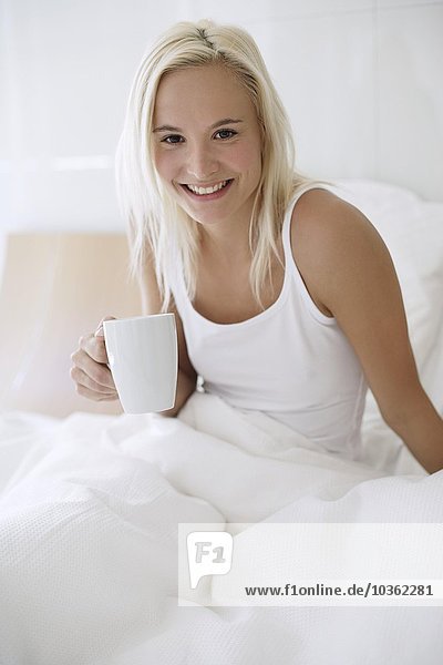 Frau trinkt Tee im Bett