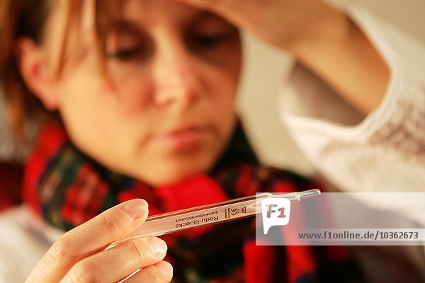 Gesundheit  Kälte  Krankheit. Junge Frau misst ihre Blutwärme mit einem Fieberthermometer