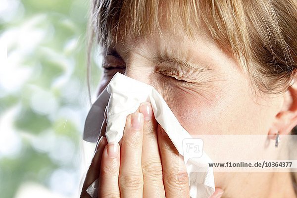 Junge erwachsene Frau hat Schnupfen  muss niesen  putzt sich die Nase mit einem Taschentuch