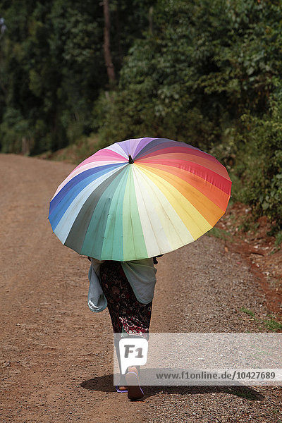 Frau geht auf einer Landstraße und trägt einen Regenschirm
