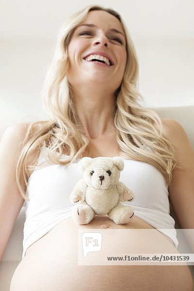 MODELL FREIGEGEBEN. Schwangere Frau mit einem Teddybär auf ihrem Bauch. Sie ist im 8. Monat schwanger.