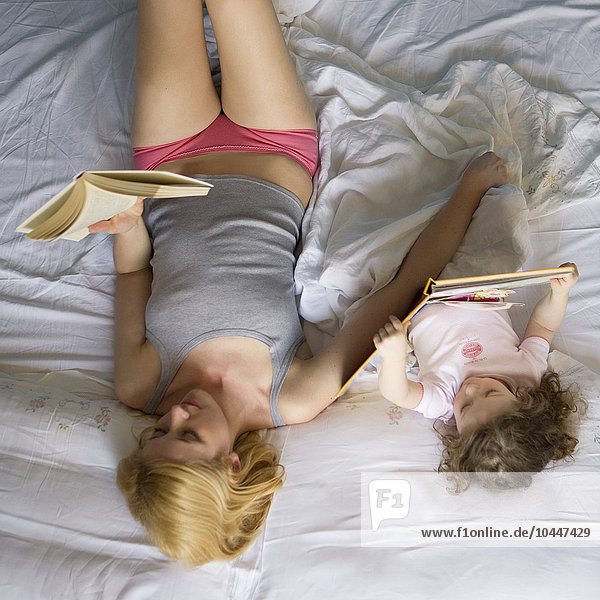 Mutter und Tochter auf dem Bett liegend  lesend