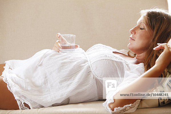 schwangere Frau mit einem Glas Wasser auf der Couch