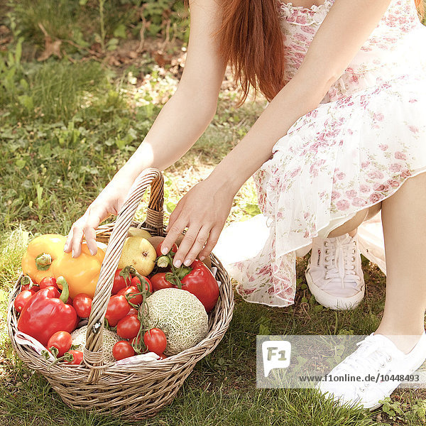 Hände einer Frau auf einem Korb mit Gemüse in einem Garten