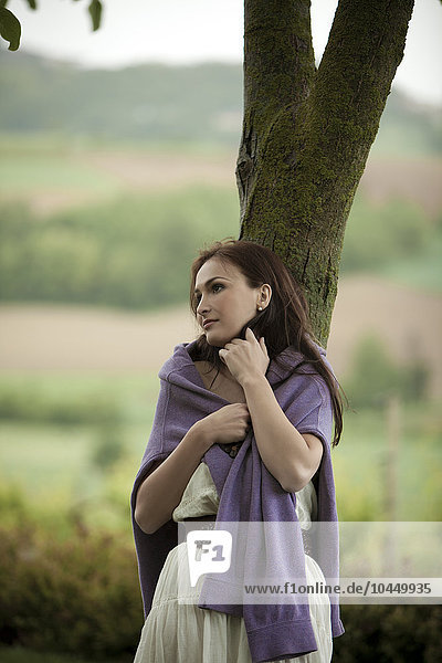 woman leaning against a tree in the countryside