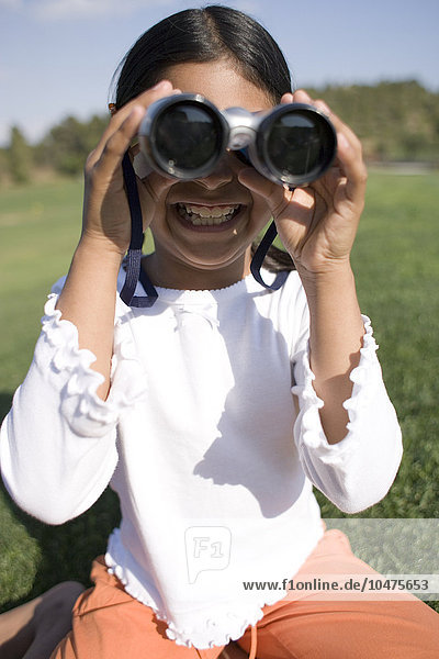 MODEL RELEASED. Girl using binoculars. Binoculars contain magnifying lenses that are used to view distant objects. Girl using binoculars