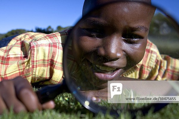 MODEL RELEASED. Boy using a magnifying glass to examine an area of grass. Boy using a magnifying glass