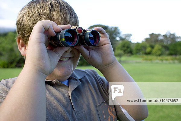 MODEL RELEASED. Boy using binoculars in a park. Boy using binoculars