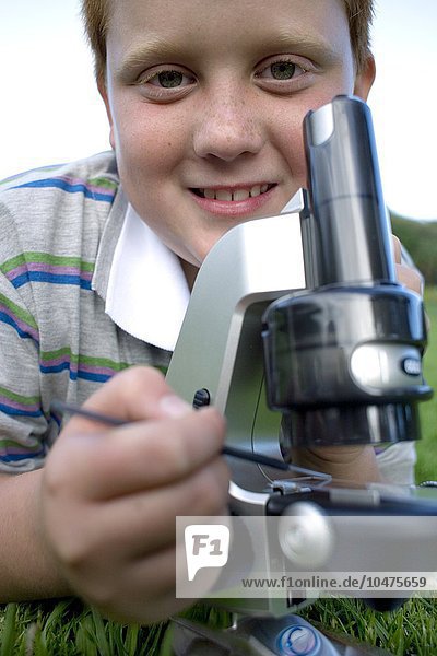 MODELL FREIGEGEBEN. Junge  der ein Lichtmikroskop benutzt  um ein Exemplar zu untersuchen Junge  der ein Lichtmikroskop benutzt