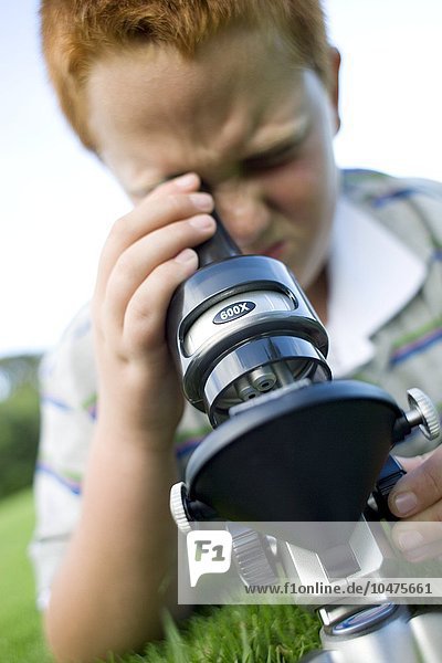 MODELL FREIGEGEBEN. Junge  der ein Lichtmikroskop benutzt  um ein Exemplar zu untersuchen Junge  der ein Lichtmikroskop benutzt