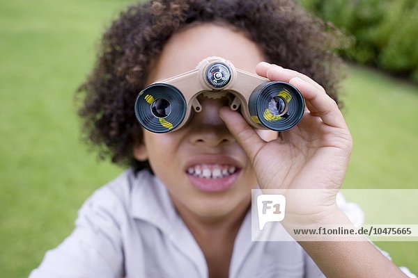 MODEL RELEASED. Boy using binoculars in a park. Binoculars contain magnifying lenses that are used to view distant objects. Boy using binoculars
