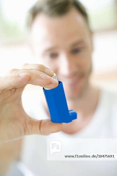 MODELL FREIGEGEBEN. Verwendung eines Asthma-Inhalators. Ein Mann verwendet einen Inhalator zur Behandlung eines Asthmaanfalls. Der Inhalator enthält bronchienerweiternde Medikamente  die die verengten Atemwege in der Lunge erweitern. Asthma-Inhalator