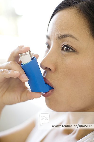 MODELL FREIGEGEBEN. Verwendung eines Asthma-Inhalators. Eine Frau verwendet einen Inhalator zur Behandlung eines Asthmaanfalls. Der Inhalator enthält bronchienerweiternde Medikamente  die die verengten Atemwege in der Lunge erweitern. Asthma-Inhalator