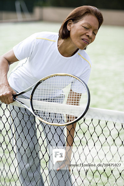 MODEL RELEASED. Painful knee injury. Woman holding her knee in pain during a game of tennis. She may have damaged the joint while hitting the ball. The action of hitting a tennis ball causes the body to rotate around the hips and knees  putting a great deal of strain on these joints. Long-term repetition of an incorrect action can cause chronic injuries to the joints. Painful knee injury