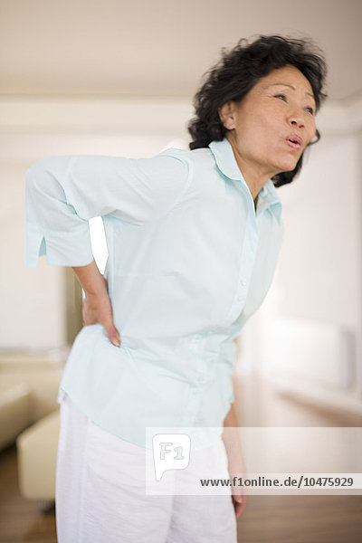 MODELL FREIGEGEBEN. Schmerzen im unteren Rücken. Frau  die ihren schmerzenden unteren Rücken hält. Rückenschmerzen sind ein sehr häufiges Leiden  das am häufigsten die Lendenwirbelsäule (den unteren Teil des Rückens) betrifft. Die Schmerzen sind auf eine Schädigung  meist eine Zerrung  der Weichteile (Muskeln und Bänder) um die Wirbelsäule zurückzuführen. Die Behandlung umfasst Ruhe und schmerzstillende Medikamente. Rückenschmerzen