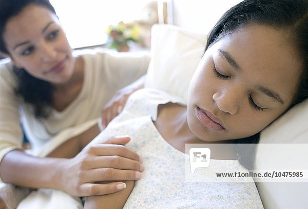 MODELL FREIGEGEBEN. Besuch im Krankenhaus. Mutter hält die Hand ihrer Tochter  während sie in einem Krankenhausbett schläft Krankenhausbesuch
