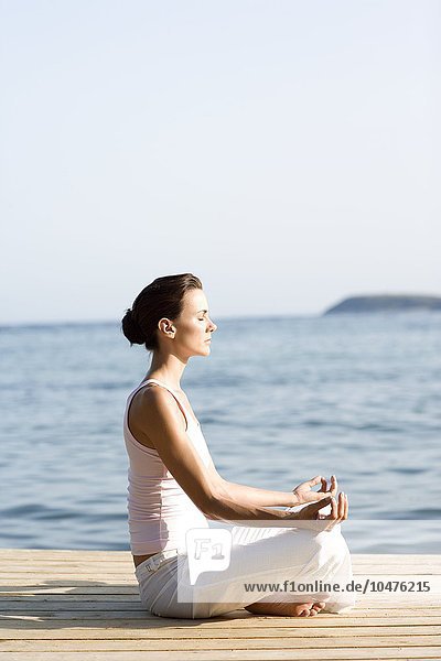 MODELL FREIGEGEBEN. Frau führt eine Yoga-Übung am Meer durch Frau führt Yoga-Übung durch