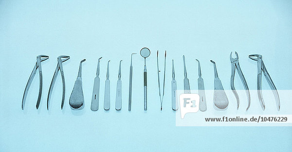 In einer Reihe angeordnete zahnärztliche Ausrüstung. Ganz rechts und ganz links befinden sich zwei Zangensets zum Entfernen von Zähnen. In der Mitte befinden sich ein Winkelspiegel zum Betrachten der Zähne und eine Pinzette. Bei den übrigen Werkzeugen handelt es sich um verschiedene Arten von Schabern und Picks zur Überprüfung der Unversehrtheit der Zähne und zur Entfernung von Plaque. Zahnärztliche Ausrüstung