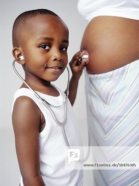 MODELL FREIGEGEBEN. Schwangere Frau und Sohn. 4 Jahre alter Junge  der mit einem Stethoskop den Herzschlag seines Geschwisters abhört. Seine Mutter ist in der 30. Woche schwanger. Eine Schwangerschaft dauert zwischen 37 und 42 Wochen. Schwangere Frau und Sohn