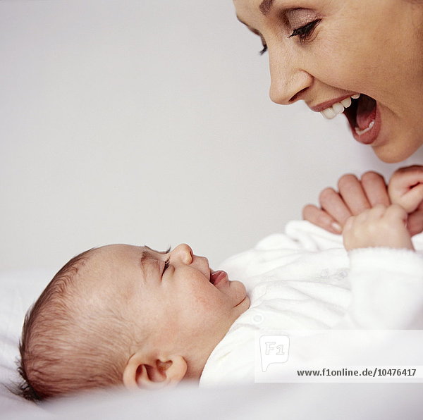 MODEL RELEASED. Mother and baby girl. Mother and her 12-week-old baby girl smiling as they look at each other. Babies recognise and respond to human faces from a very early age. Mother and baby girl