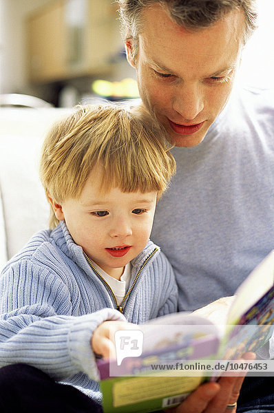 MODELL FREIGEGEBEN. Vaterschaft. Vater liest ein Buch mit seinem dreijährigen Sohn Vaterschaft
