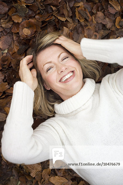 MODELL FREIGEGEBEN. Lächelnde Frau auf Herbstblättern liegend Lächelnde Frau auf Herbstblättern liegend
