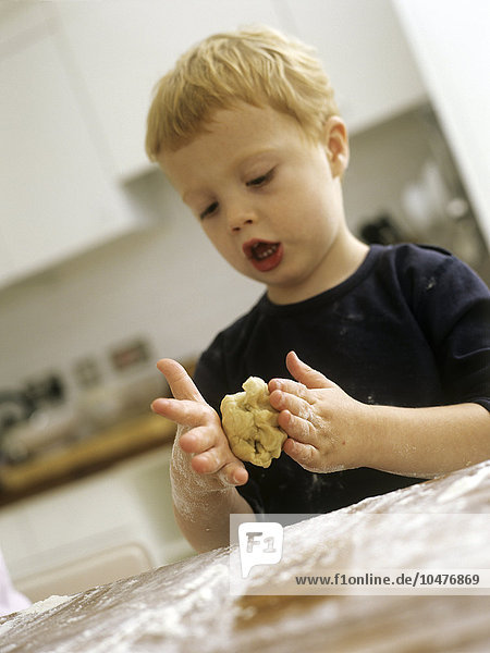MODELL FREIGEGEBEN. Kekse backen. Ein dreijähriger Junge singt  während er einen Keksteig ausrollt Kekse backen