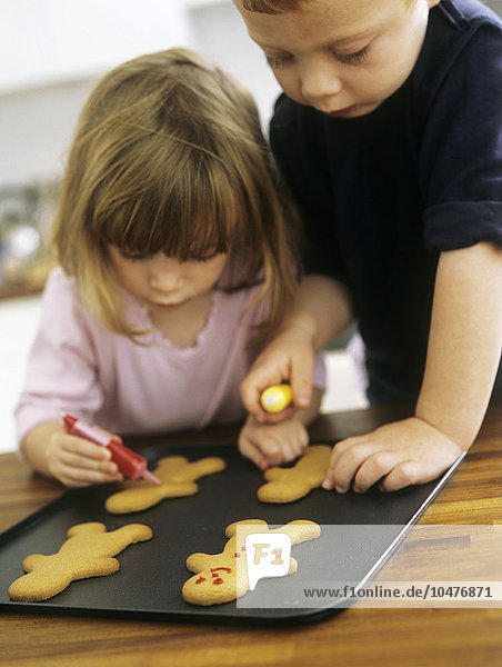 MODELL FREIGEGEBEN. Kekse backen. Zwei dreijährige Kinder verzieren frisch gebackene Kekse mit farbigem Zuckerguss Kekse backen