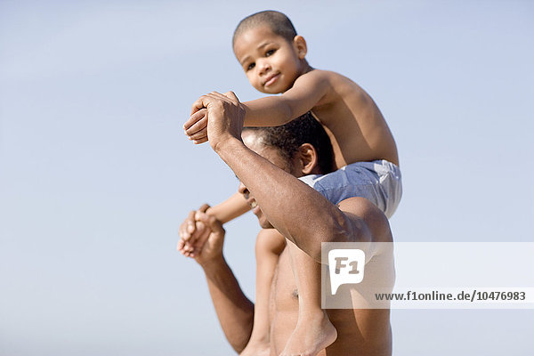 MODELL FREIGEGEBEN. Vater und Sohn. Junge wird auf den Schultern seines Vaters am Strand getragen Vater und Sohn